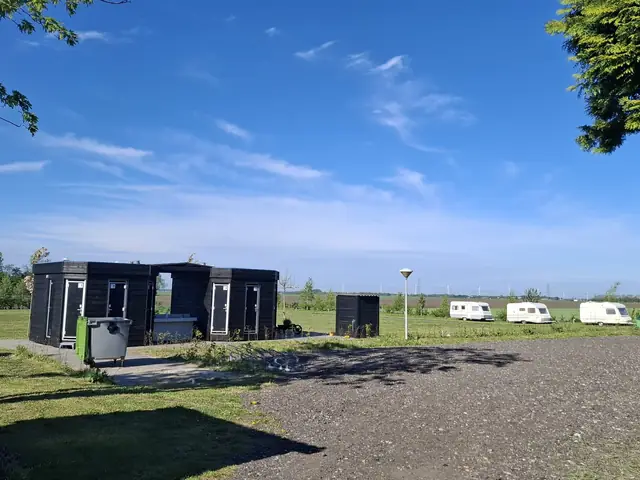 Sanitairgebouwen en caravans op het kampeerveld onder een blauwe lucht